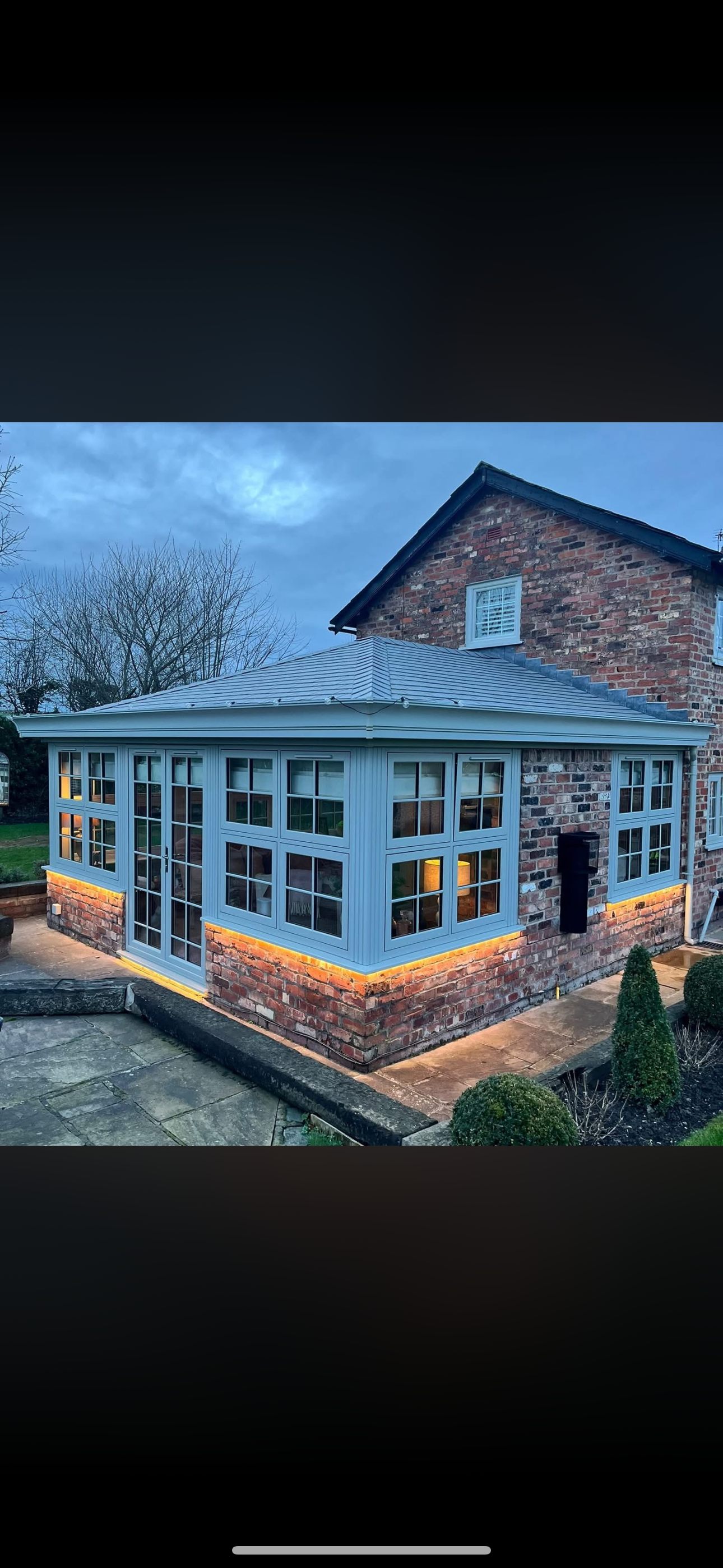 Conservatory extension lit at dusk with warm LED soffit and plinth lighting glowing against a deep blue evening sky