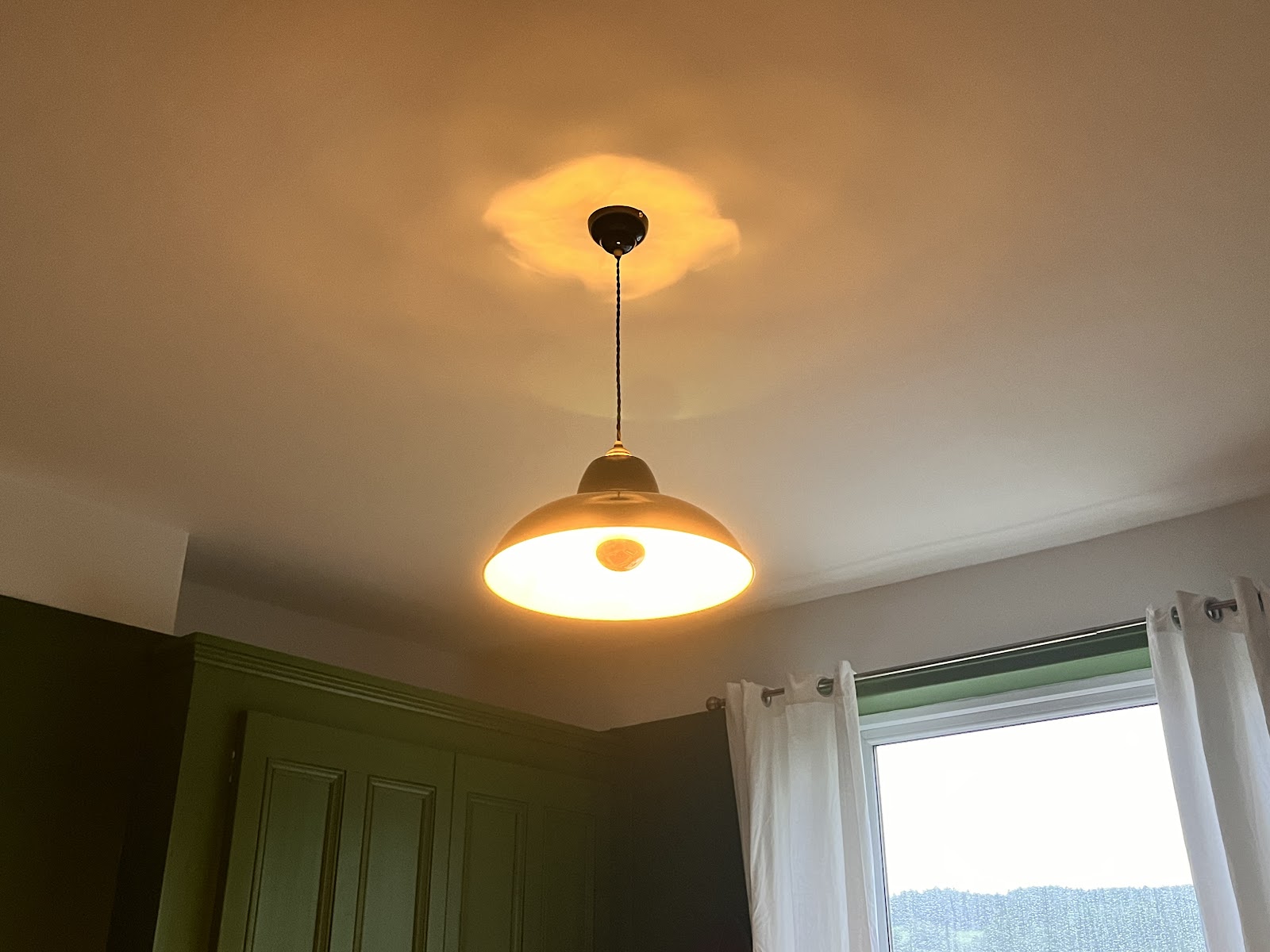 Bedroom with a warm pendant light fitting glowing above a green fitted wardrobe